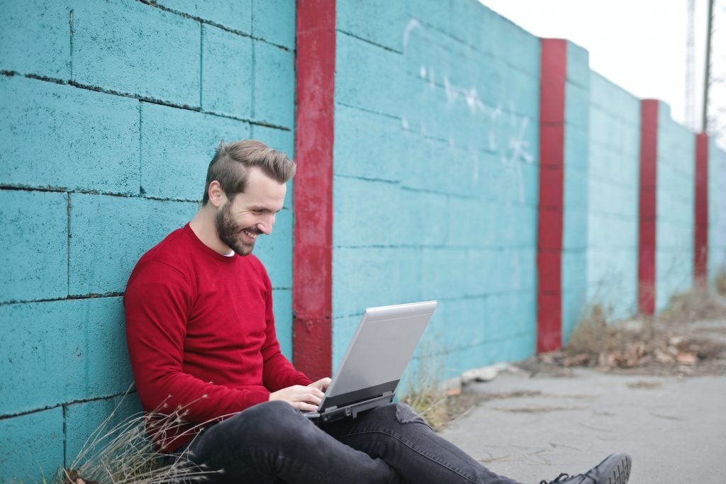 man leaning against wall using laptop 941572
